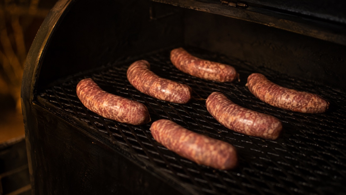 Raw sausage links spaced on a smoker grate with no smoke, casings drying