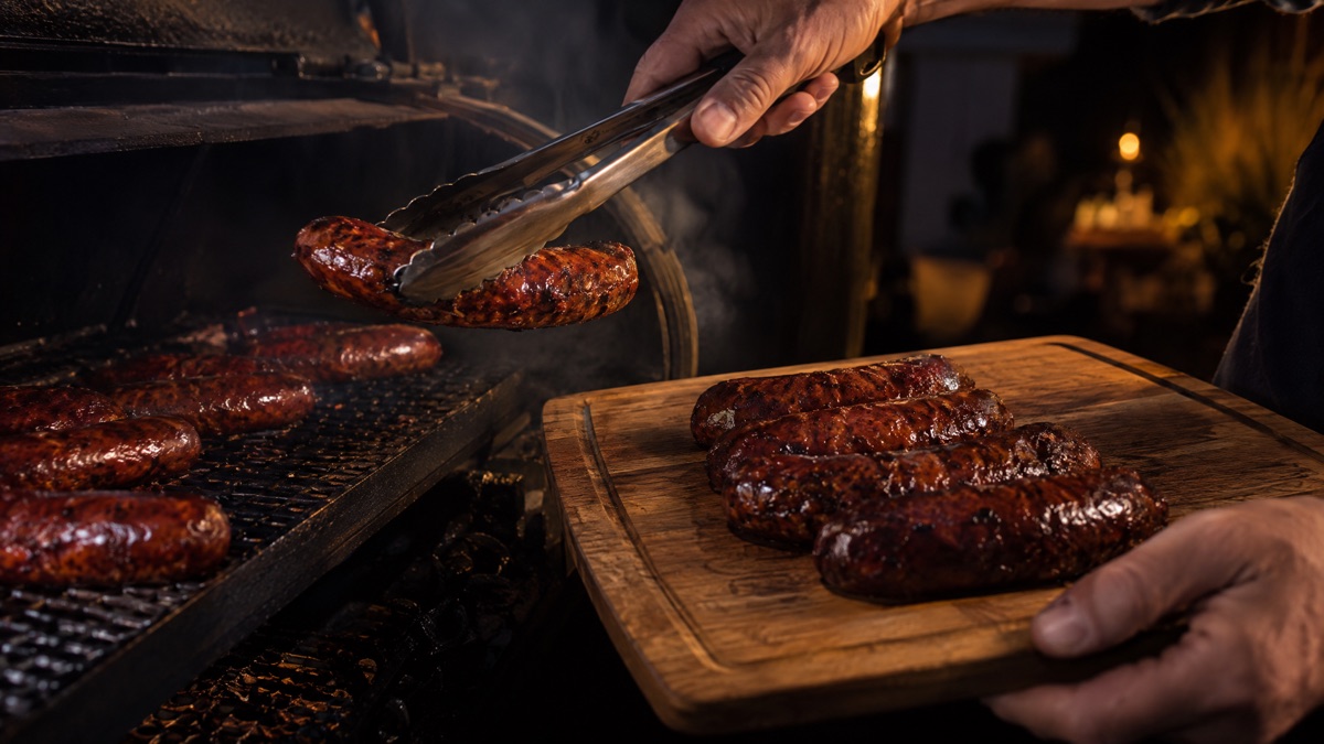 Tongs lifting finished smoked sausage links off a smoker grate
