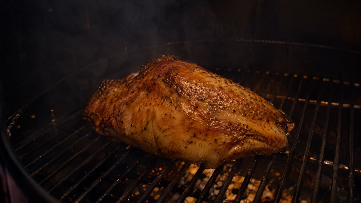 A turkey breast on a smoker grate with the skin tightened and turned golden