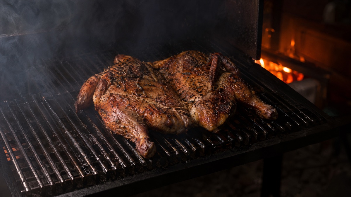 A spatchcocked chicken lying flat skin side up on a smoker grate