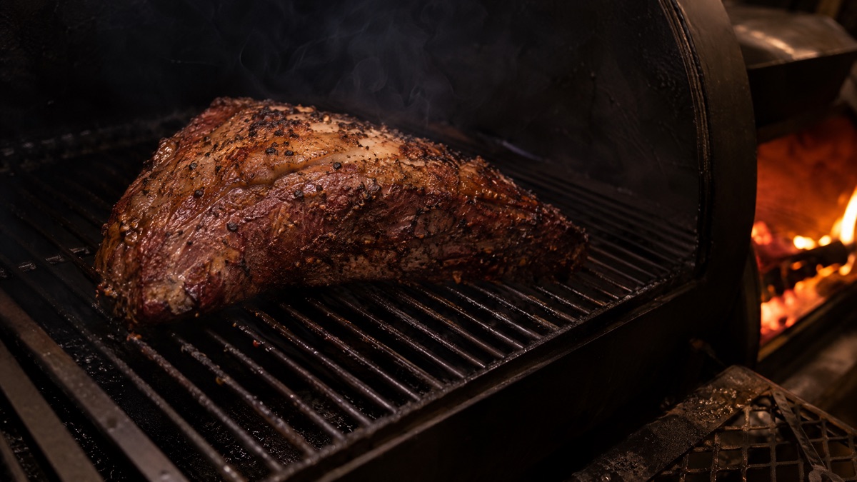A seasoned tri-tip set fat cap up on a smoker grate