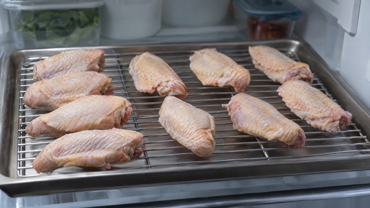 Raw chicken wings spaced on a rack, uncovered, inside a refrigerator