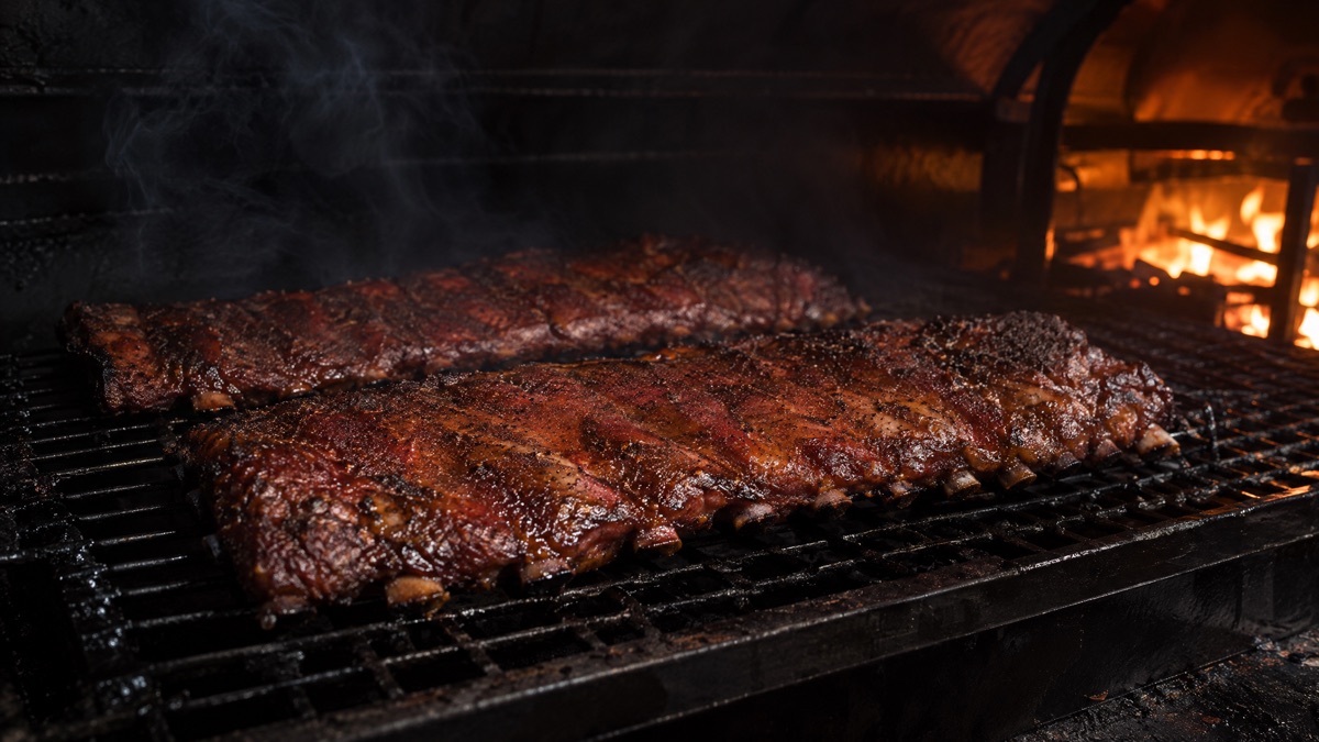 Two racks of St. Louis cut pork ribs bone side down on a smoker grate with mahogany bark